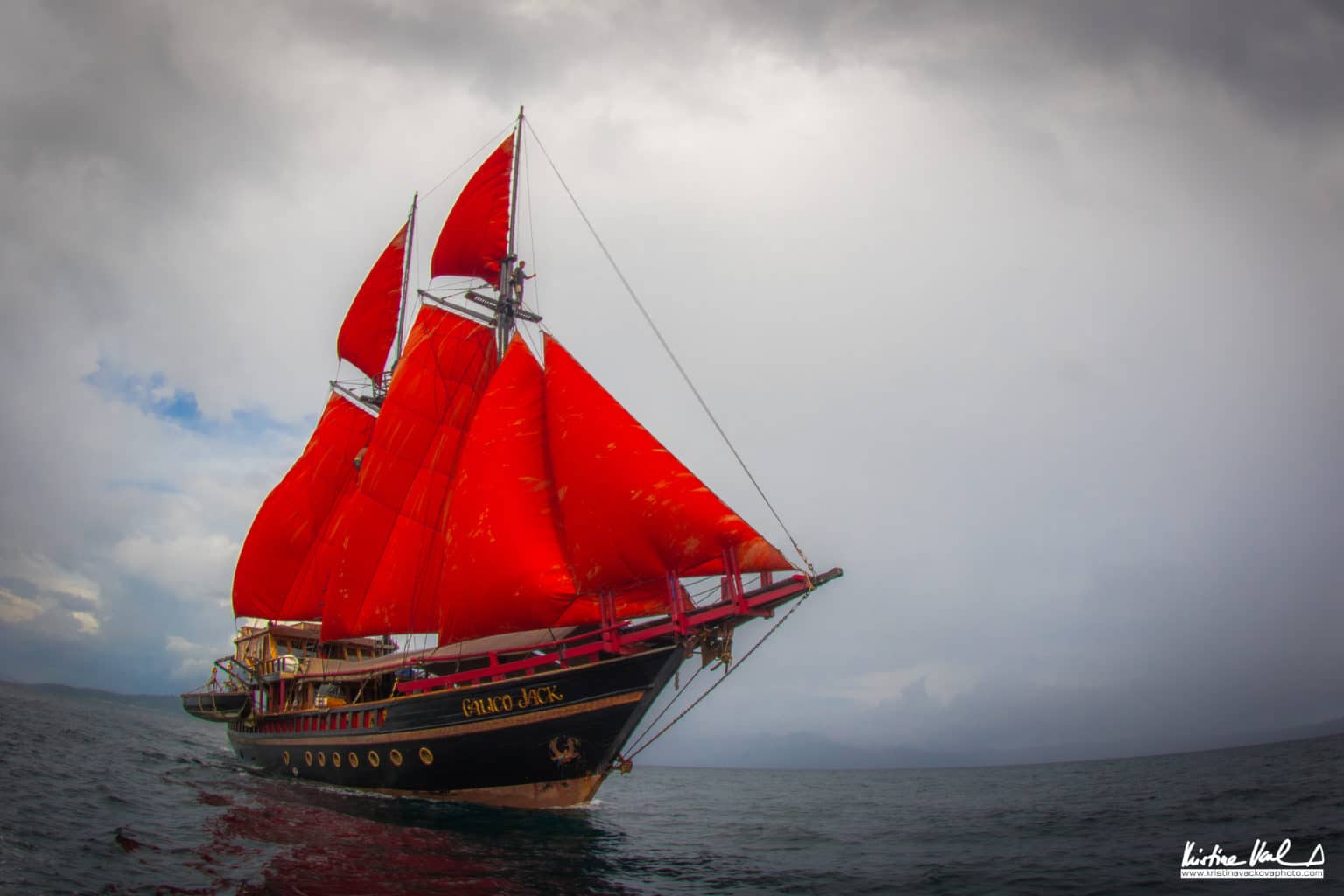 The vivid red sails of the Calico Jack Phinisi against an overcast sky
